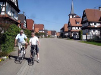 Ein elsässisches Dorf, an dem zwei Radfahrer am Straßenrand stehen