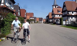Zwei Radler stehen in einem Dorf mit Fachwerkhäusern im Elsass am Straßenrand