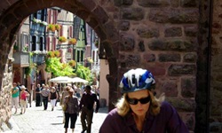 Blick auf ein ehemaliges Stadttor des verlockenden Elsass und deren dahinterliegende Fußgängerzone. Im Vordergrund radelt eine Frau.