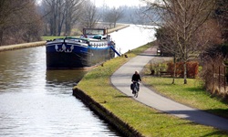 Ein Fahrradfahrer fährt auf einem Weg neben einem Fluss, auf dem ein Schiff anglegt ist, im Elsass entlang