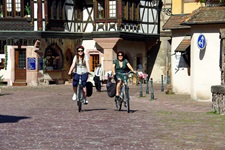 Blick auf eine Straße mit zwei Radlerinnen in einem elsässischen Dorf mit Fachwerk