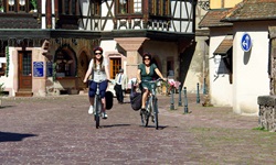 Blick auf eine Straße mit zwei Radlerinnen in einem elsässischen Dorf mit Fachwerk