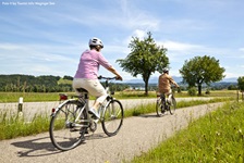 Zwei Radfahrer radeln auf dem Benedikt-Radweg auf den Waginger See zu.