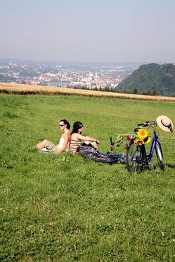 Zwei Radlerinnen sitzen Rücken an Rücken in einer Wiese und genießen ihre Pause.