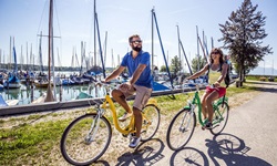 Ein Radfahrerpärchen passiert den Chiemsee, auf dem zahlreiche Boote schaukeln.
