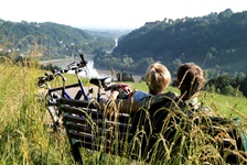 Ein Radlerpärchen sitzt auf einer Bank und genießt den Blick über die Donau.