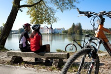 Ein Radlerpärchen hat seine Räder abgestellt und blickt von einer hölzernen Bank aus auf die Donau.