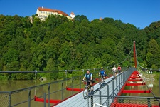 Zwei Radler fahren unterhalb der Passauer Festung Oberhaus auf einer Stahlbrücke über die Donau.