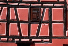 Blick auf eine typische elsässische Fachwerkhausfassade, die in rötlichem Ton gestrichen ist