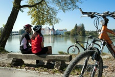 Ein Radfahrerpärchen macht auf einer Bank am Innufer Pause.