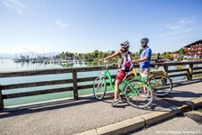 Ein Radfahrerpärchen steht auf einer Brücke und genießt den schönen Ausblick über den Chiemsee.