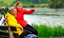 Zwei Radfahrer machen Pause auf einer Bank am Ufer der Donau