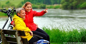 Zwei Radfahrer machen Pause auf einer Bank am Ufer der Donau