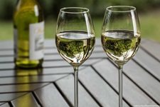 Zwei mit Weißwein gefüllte Gläser stehen zusammen mit der Weinflasche auf einem Holztisch.
