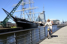 Eine Radlerin fährt über eine Brücke in den Hafen von Bremerhaven - im Hintergrund das Restaurantschiff "Seute Deern" und das wie ein Schiff geformte Gebäude des Deutschen Schifffahrtsmuseums.