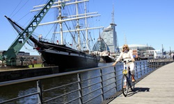 Eine Radlerin fährt über eine Brücke in den Hafen von Bremerhaven - im Hintergrund das Restaurantschiff "Seute Deern" und das wie ein Schiff geformte Gebäude des Deutschen Schifffahrtsmuseums.