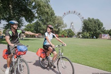 Ein Radlerpärchen durchquert den Prater, im Hintergrund das weltberühmte Riesenrad.