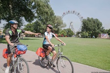 Zwei Radler radeln auf dem Donauradweg in Wien, im Hintergrund sieht man das Wiener Riesenrad