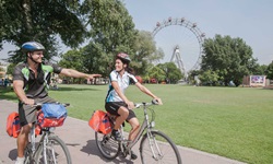 Zwei Radfahrer radeln den Donau-Radweg in Wien entlang, im Hintergrund ist das Riesenrad von Wien zu sehen