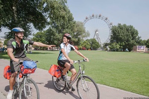 Ein Radlerpaar radelt in Wien auf dem Donau-Radweg, im Hintergrund das Riesenrad von Wien