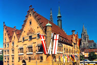 Der Prinzipalmarkt in Münster mit seinen charakteristischen Giebelhäusern, den bunten Fahnen und dem historischen Rathaus im Hintergrund.