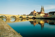 Die Steinerne Brücke in Regensburg, die sich über die Donau spannt und als Spiegelung im ruhigen Wasser zu sehen ist.