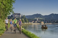 Radfahrer auf dem Donau-Radweg in Österreich mit malerischem Blick auf die Donau und eine Burg im Hintergrund