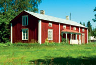 Traditionelles rotes Holzhaus mit weißen Verzierungen vor der Kulisse aus grünen Wiesen und Bäumen und Smaland, Schweden