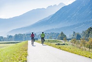 Zwei Radfahrer auf dem alsphaltierten Alpe-Adria-Radweg, die entlang einer malerischen Landschaft entlangfahren